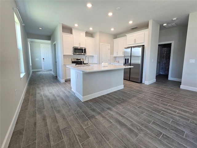 kitchen with a kitchen island with sink, appliances with stainless steel finishes, dark hardwood / wood-style flooring, and white cabinets