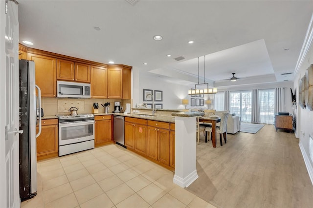 kitchen featuring appliances with stainless steel finishes, sink, a tray ceiling, kitchen peninsula, and ceiling fan