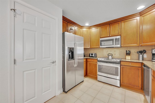 kitchen with appliances with stainless steel finishes, tasteful backsplash, light stone counters, and light tile patterned floors