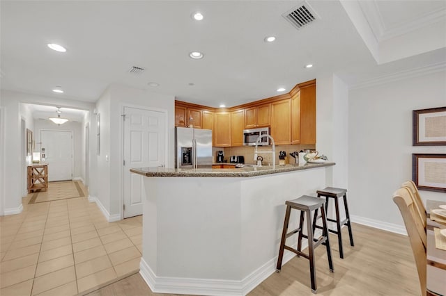 kitchen with light stone countertops, appliances with stainless steel finishes, light tile patterned flooring, kitchen peninsula, and crown molding