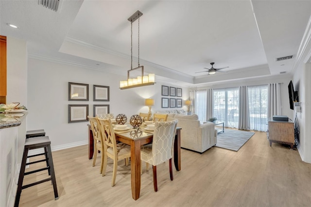 dining space featuring crown molding, a tray ceiling, light wood-type flooring, and ceiling fan