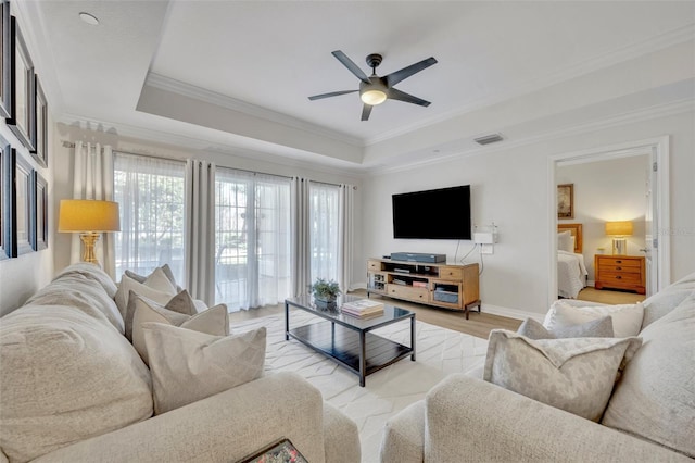 living room with light hardwood / wood-style floors, crown molding, a raised ceiling, and ceiling fan