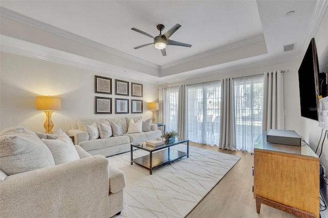 living room with a raised ceiling, crown molding, light wood-type flooring, and ceiling fan