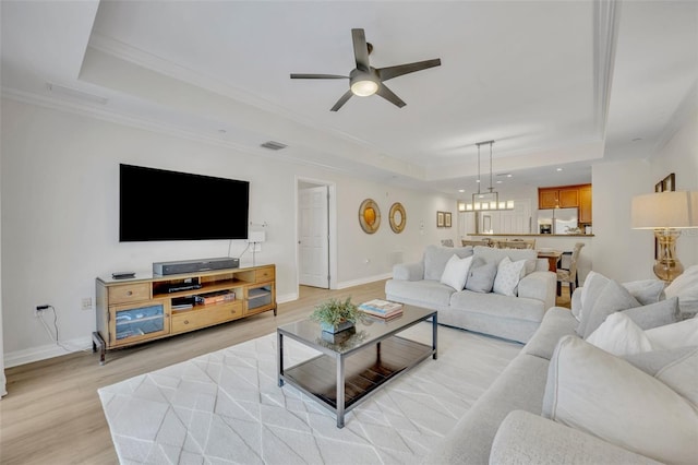 living room featuring a tray ceiling, ornamental molding, light hardwood / wood-style flooring, and ceiling fan with notable chandelier