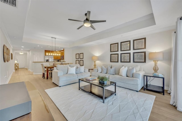 living room with light hardwood / wood-style flooring, ornamental molding, a tray ceiling, and ceiling fan with notable chandelier