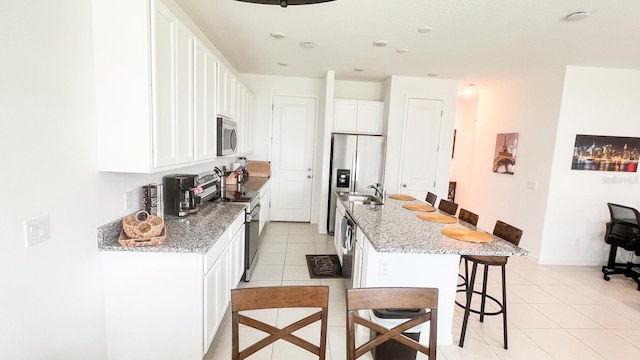 kitchen featuring light stone counters, a breakfast bar area, an island with sink, white cabinetry, and stainless steel appliances