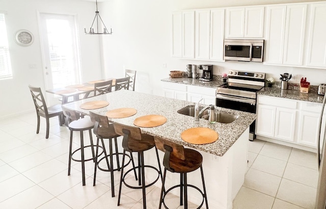 kitchen with white cabinetry, stainless steel appliances, pendant lighting, and a kitchen island with sink