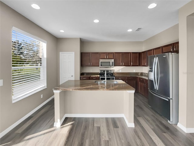 kitchen featuring an island with sink, dark brown cabinetry, stainless steel appliances, and wood-type flooring