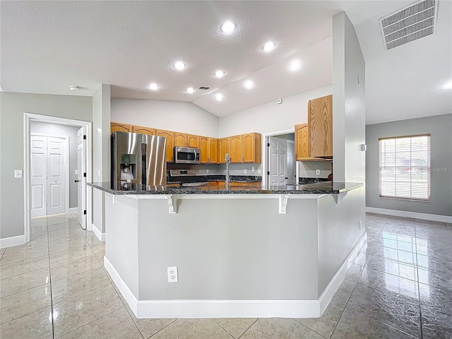 kitchen featuring kitchen peninsula, dark stone countertops, vaulted ceiling, a breakfast bar area, and appliances with stainless steel finishes