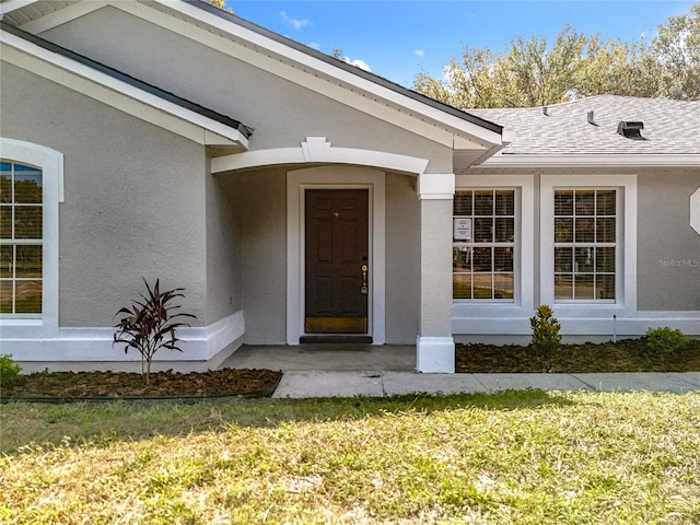 property entrance featuring a yard, roof with shingles, and stucco siding