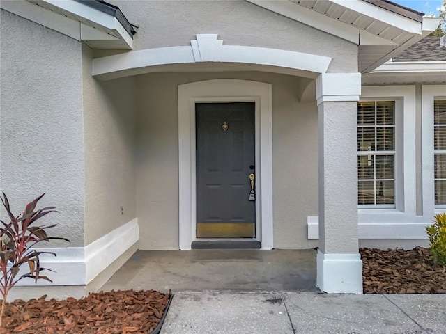 entrance to property with roof with shingles and stucco siding