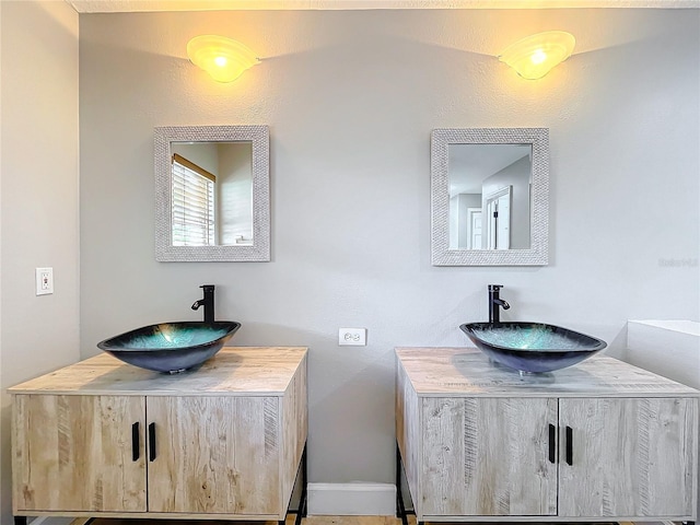 bathroom featuring two vanities, a sink, and baseboards