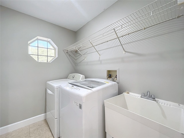 washroom featuring light tile patterned flooring, laundry area, separate washer and dryer, a sink, and baseboards