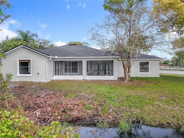 back of property with a sunroom, roof with shingles, a lawn, and stucco siding