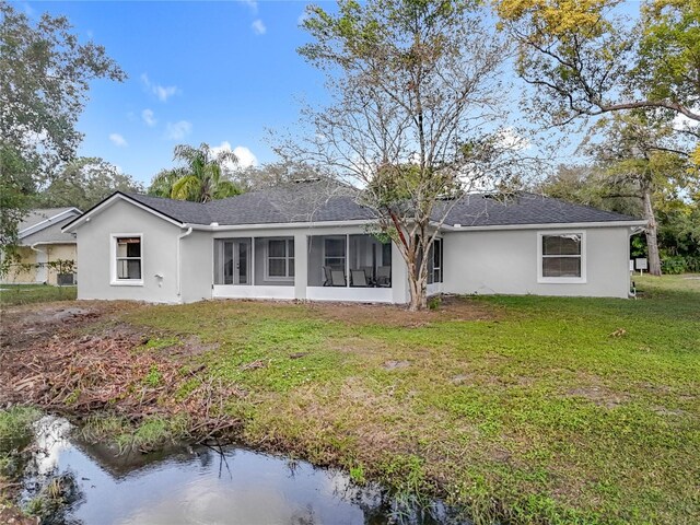 rear view of property with a sunroom, a lawn, and stucco siding