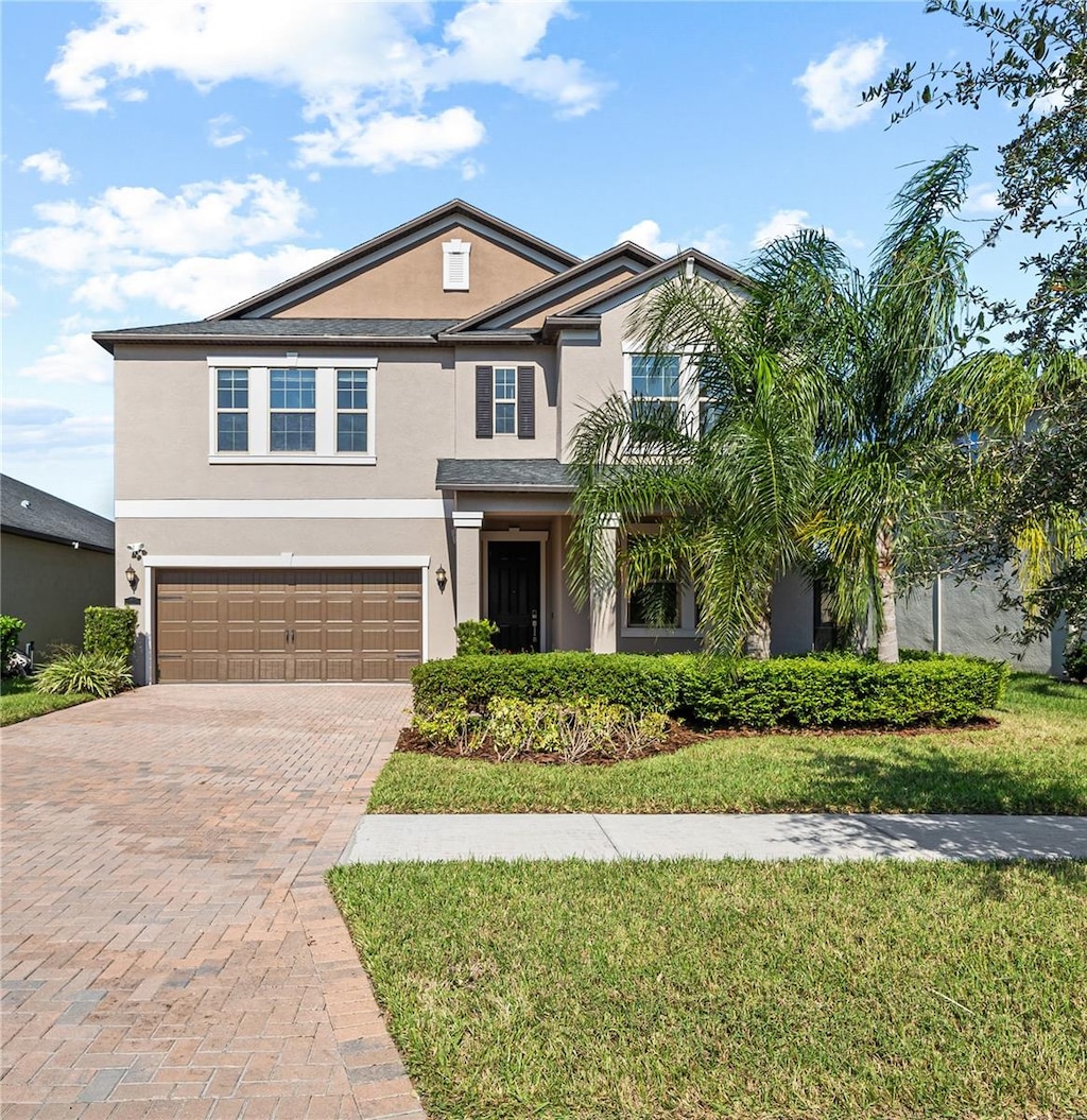 traditional home featuring an attached garage, decorative driveway, and stucco siding