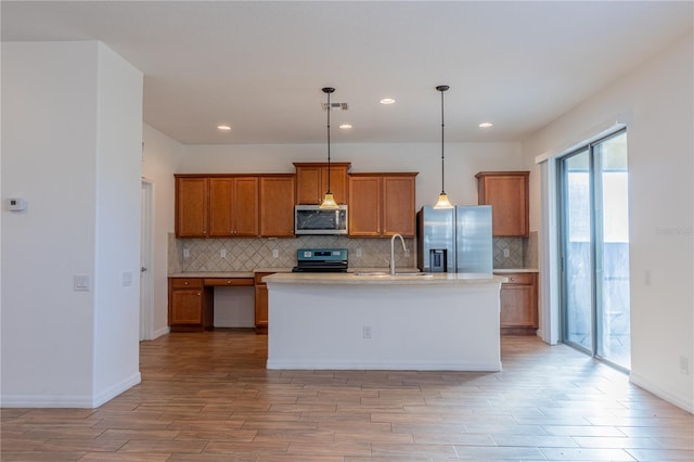 kitchen with decorative light fixtures, stainless steel appliances, a kitchen island with sink, and light hardwood / wood-style floors