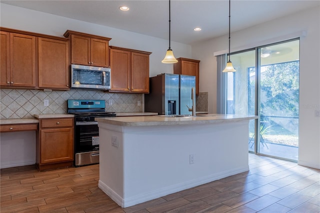 kitchen with appliances with stainless steel finishes, light wood-type flooring, hanging light fixtures, and a kitchen island with sink