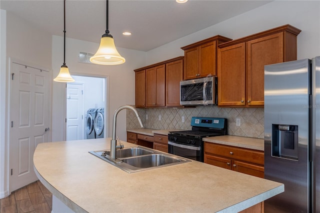 kitchen with sink, stainless steel appliances, an island with sink, decorative light fixtures, and washer and dryer