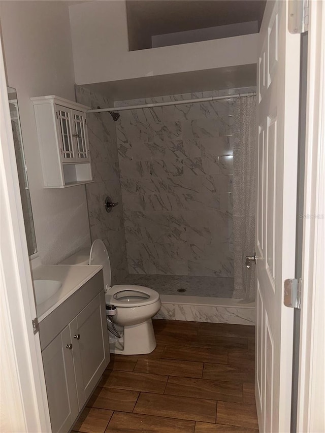 bathroom featuring a tile shower, vanity, hardwood / wood-style flooring, and toilet