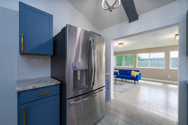 kitchen with blue cabinetry, vaulted ceiling, light hardwood / wood-style flooring, stainless steel fridge, and backsplash