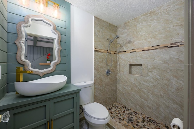 bathroom with vanity, a textured ceiling, toilet, and tiled shower