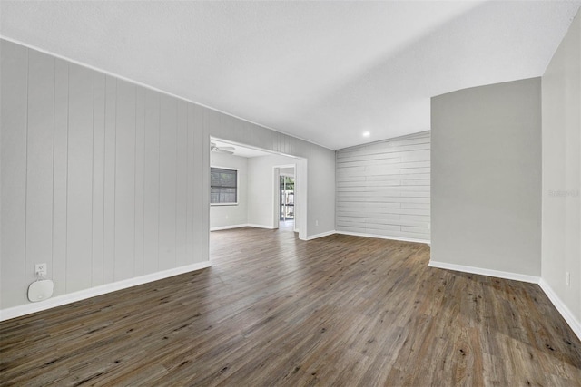 empty room featuring dark wood-type flooring, vaulted ceiling, a textured ceiling, and wood walls