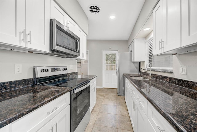 kitchen featuring appliances with stainless steel finishes, sink, dark stone counters, white cabinets, and light tile patterned floors