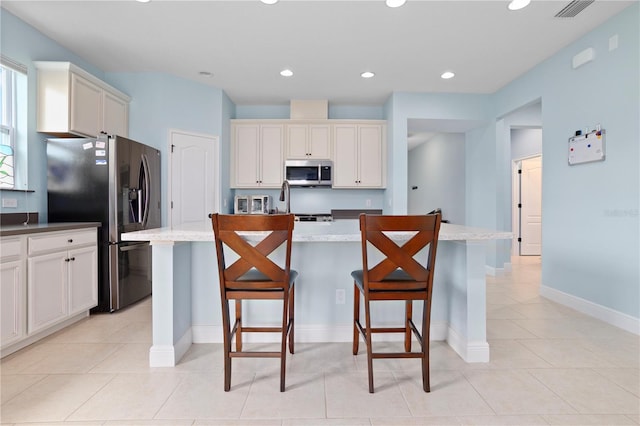 kitchen featuring appliances with stainless steel finishes, light stone counters, light tile patterned floors, a kitchen island, and a breakfast bar area