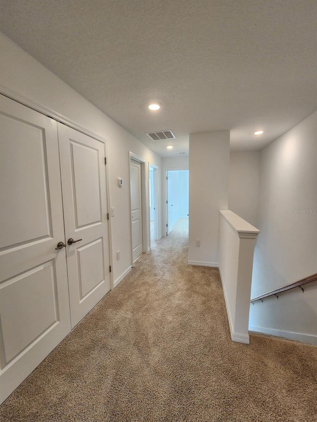 hallway featuring a textured ceiling and light colored carpet