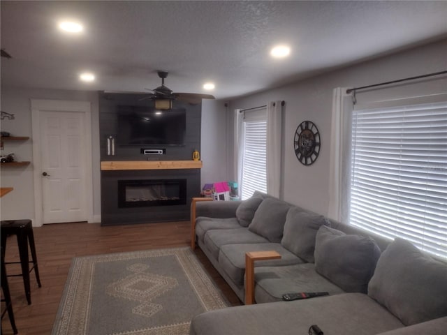 living room with a textured ceiling, wood-type flooring, a fireplace, and ceiling fan