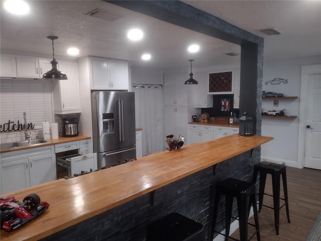 kitchen with butcher block countertops, stainless steel refrigerator with ice dispenser, and pendant lighting