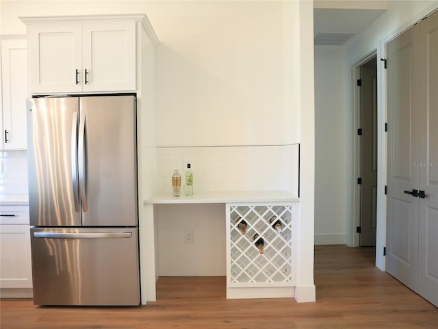 kitchen featuring tasteful backsplash, stainless steel fridge, white cabinets, and light wood-type flooring