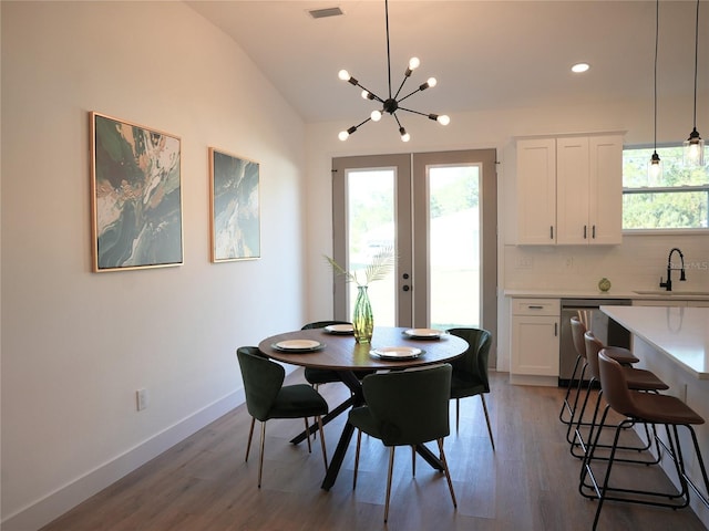 dining room featuring hardwood / wood-style floors, an inviting chandelier, french doors, sink, and vaulted ceiling