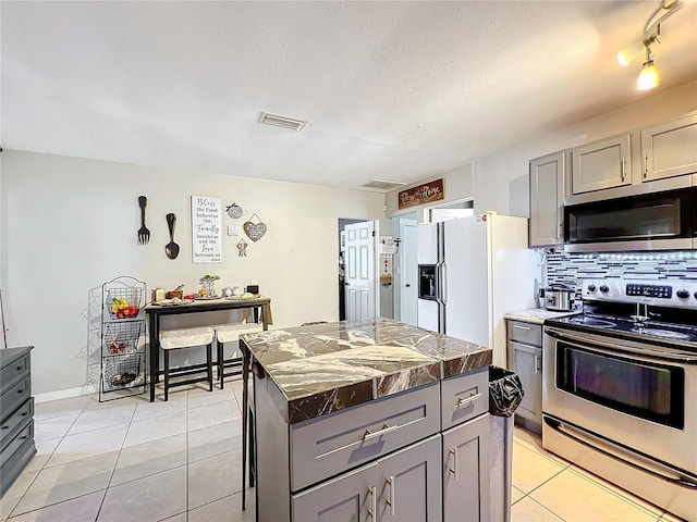 kitchen featuring gray cabinetry, stainless steel appliances, a center island, light tile patterned floors, and tasteful backsplash