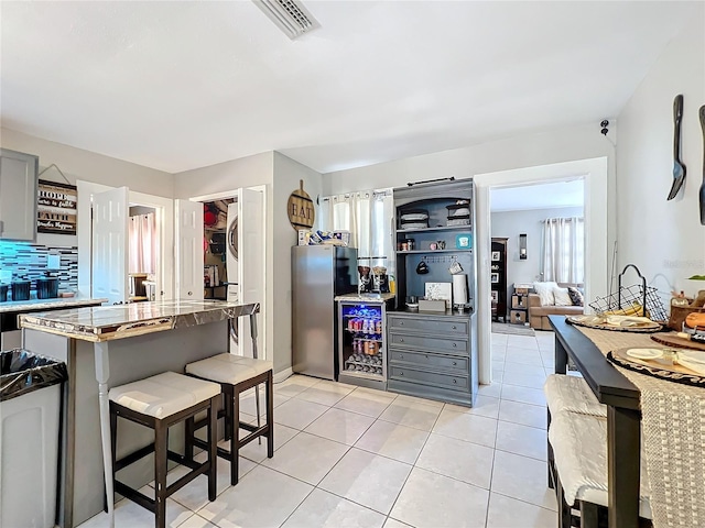 kitchen featuring stacked washer and clothes dryer, a kitchen bar, light tile patterned floors, gray cabinets, and stainless steel refrigerator