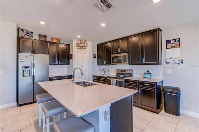 kitchen featuring an island with sink, appliances with stainless steel finishes, a kitchen bar, dark brown cabinetry, and sink