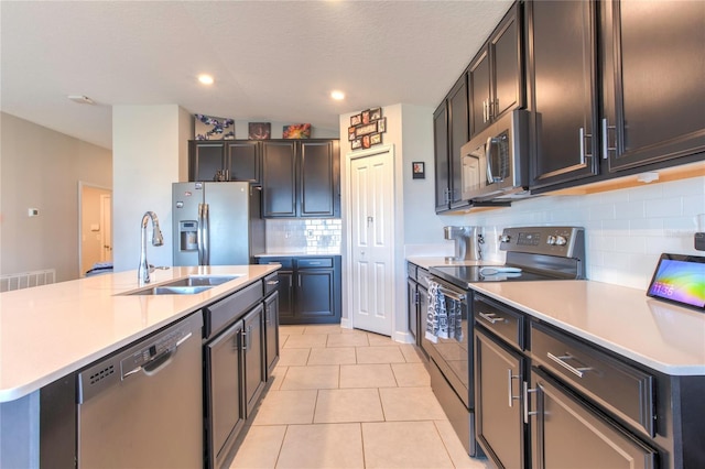 kitchen featuring decorative backsplash, a center island with sink, sink, light tile patterned flooring, and appliances with stainless steel finishes