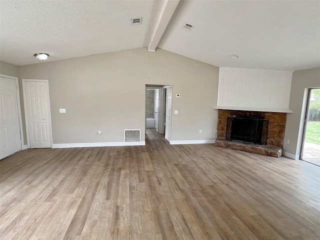 unfurnished living room featuring light hardwood / wood-style floors, a textured ceiling, a stone fireplace, and vaulted ceiling with beams