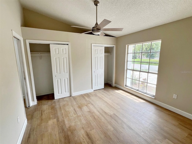 unfurnished bedroom featuring two closets, ceiling fan, a textured ceiling, vaulted ceiling, and light hardwood / wood-style floors