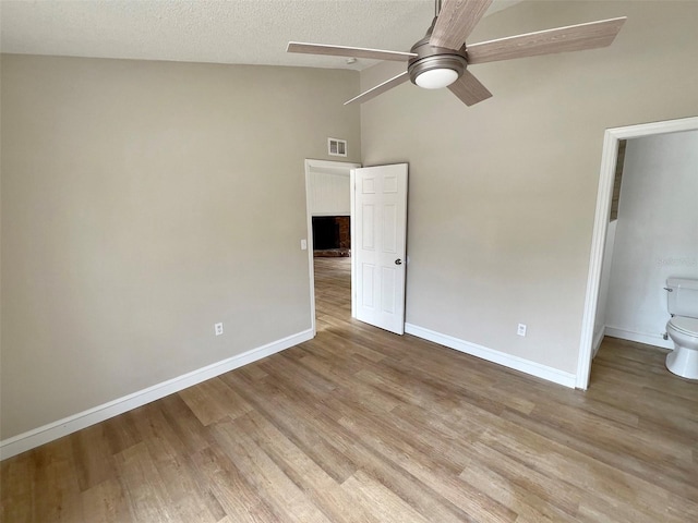 unfurnished bedroom with ceiling fan, a textured ceiling, high vaulted ceiling, connected bathroom, and light hardwood / wood-style flooring