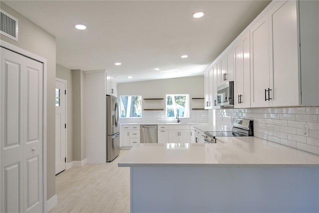 kitchen with kitchen peninsula, white cabinetry, stainless steel appliances, and light wood-type flooring