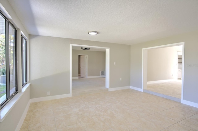 unfurnished room featuring a textured ceiling, light tile patterned floors, and plenty of natural light