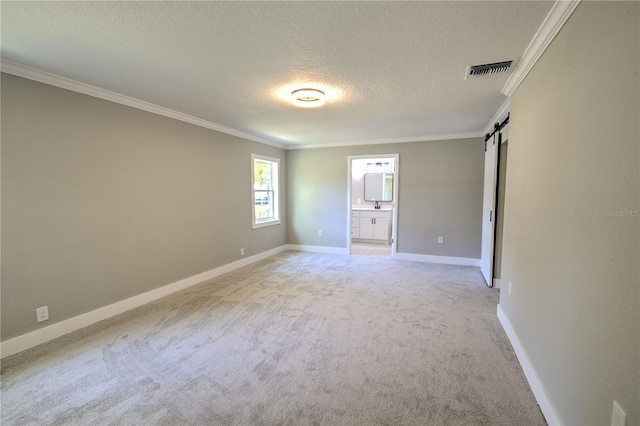 spare room featuring ornamental molding, a textured ceiling, a barn door, and light colored carpet