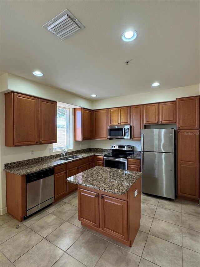 kitchen featuring sink, light tile patterned flooring, a kitchen island, stainless steel appliances, and dark stone counters