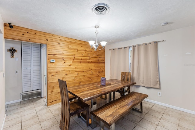 dining room with wooden walls, a textured ceiling, a chandelier, and light tile patterned floors