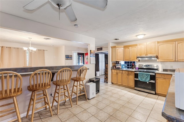 kitchen featuring a breakfast bar, stainless steel electric range oven, light tile patterned floors, light brown cabinetry, and ceiling fan with notable chandelier