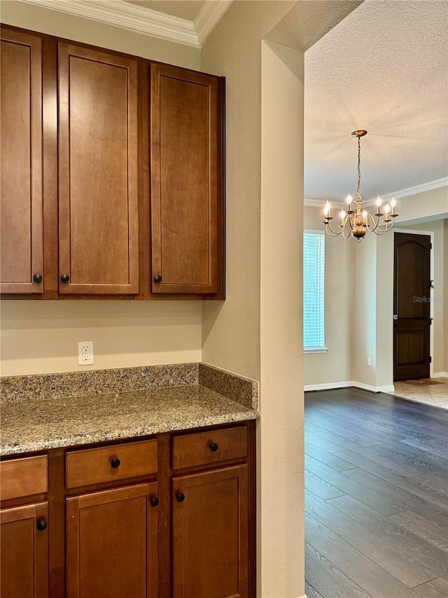 kitchen with light stone counters, a textured ceiling, crown molding, a chandelier, and light hardwood / wood-style floors