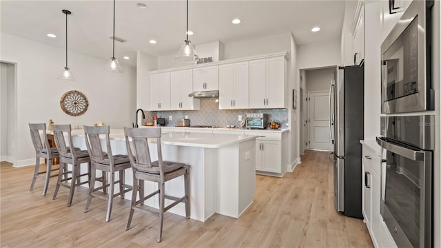 kitchen with tasteful backsplash, stainless steel appliances, under cabinet range hood, light countertops, and white cabinets