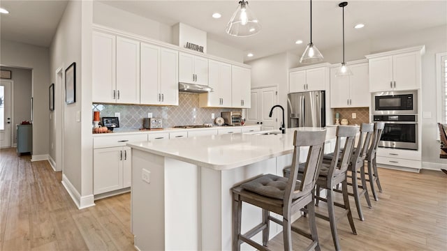 kitchen featuring a sink, decorative backsplash, stainless steel appliances, under cabinet range hood, and white cabinetry